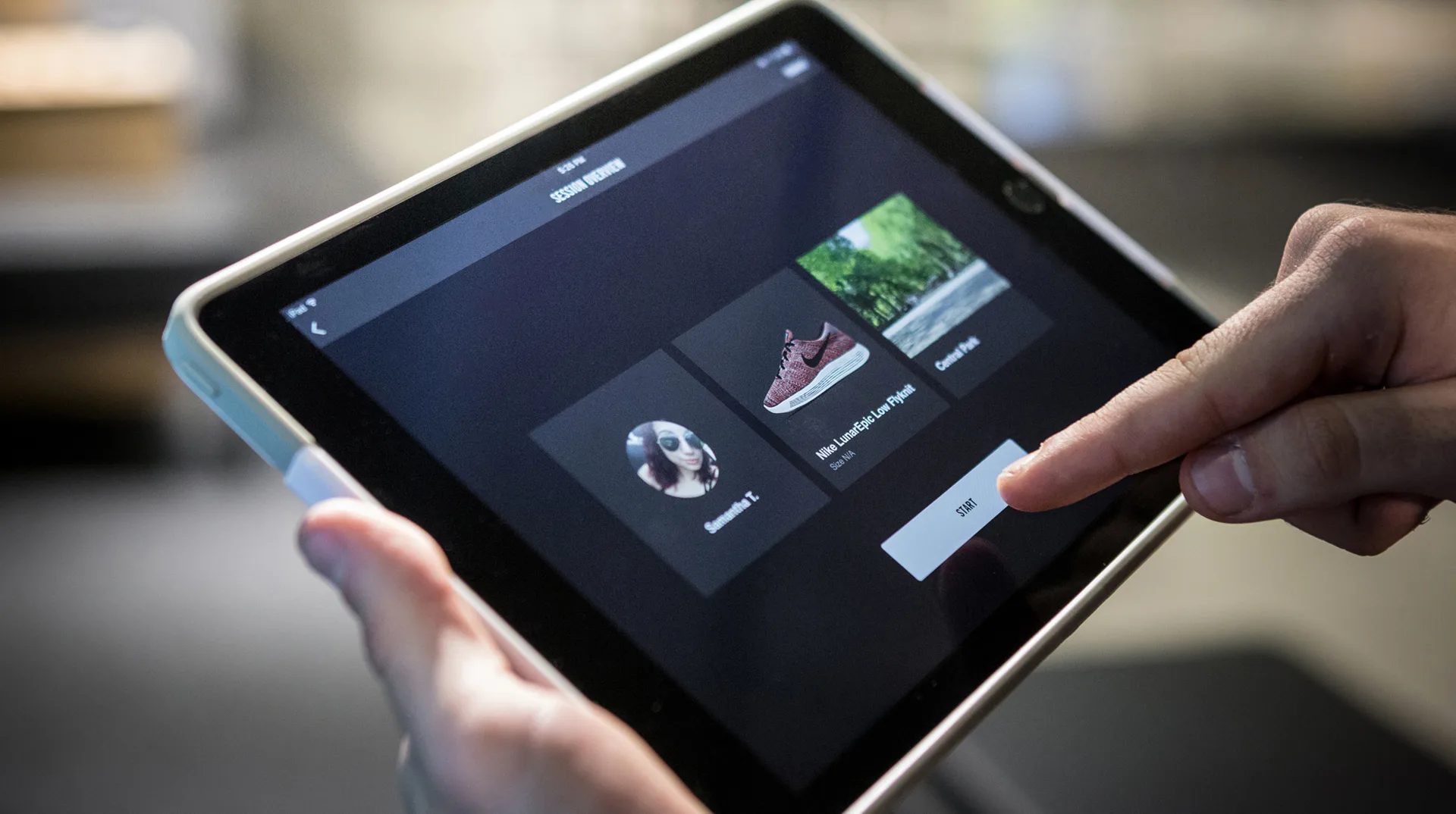 A person uses a tablet, tapping the screen to select a shoe product from a digital menu that displays two shoe options and a profile photo.