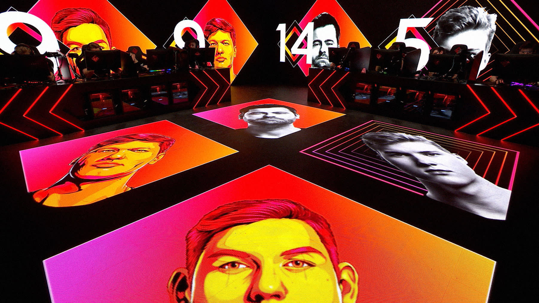 A vibrant esports stage features players at computer stations surrounded by large, colorful digital portraits and numbers, creating an intense gaming atmosphere with dramatic red, orange, and yellow lighting.