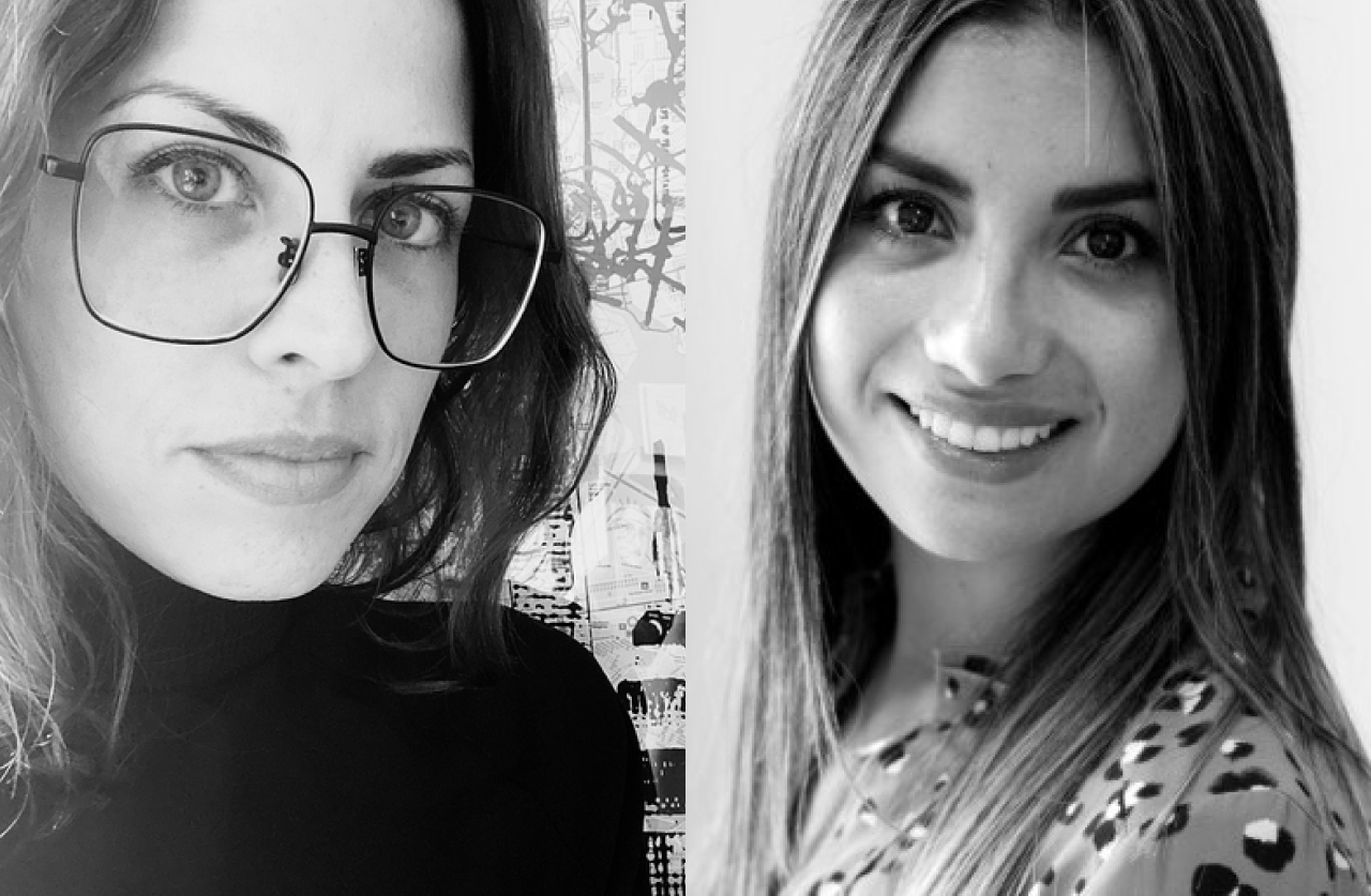 Black and white photo of two women side by side; the woman on the left wears glasses and a dark top, while the woman on the right has long hair and a patterned shirt, both looking at the camera and smiling slightly.
