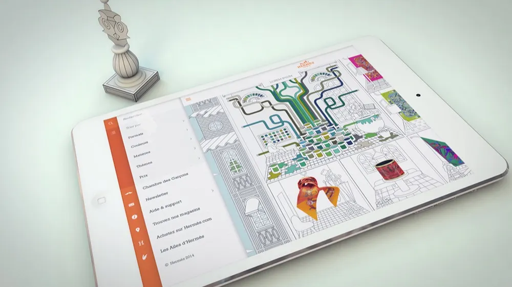 A white tablet displaying a colorful digital drawing app lies on a light surface. Next to it stands a detailed chess piece resembling a bishop. The screen shows partially colored geometric and nature-themed artwork.