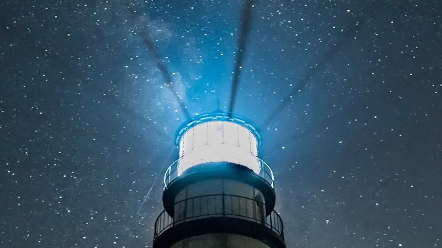A brightly lit lighthouse shines beams of light into the night sky, with countless stars and the faint band of the Milky Way visible in the background.