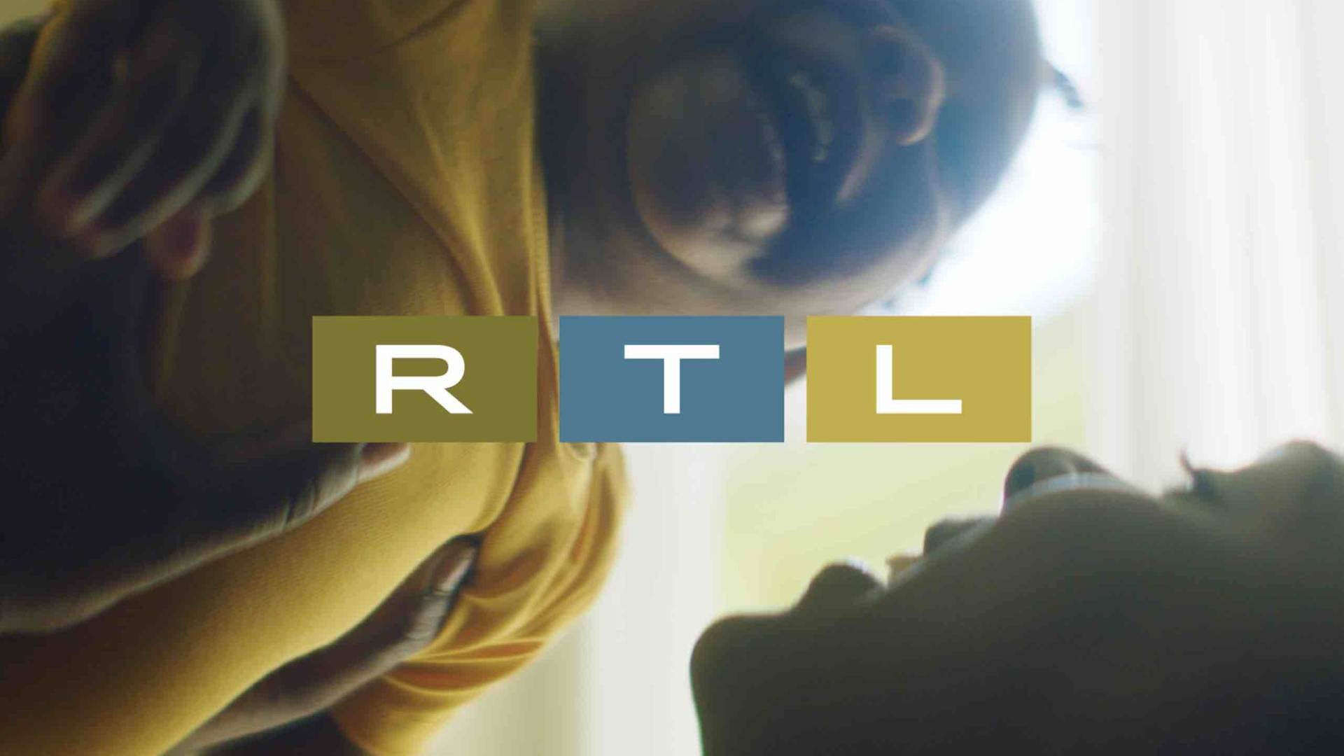 A smiling baby in a yellow shirt is held up in the air by an adult, both enjoying a playful moment. The letters R, T, and L are displayed in colored boxes over the center of the image.