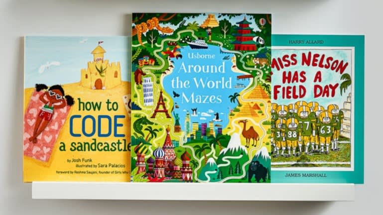 Three colorful children’s books on a white shelf: “How to Code a Sandcastle,” “Around the World Mazes,” and “Miss Nelson Has a Field Day.” Each cover features playful, vibrant illustrations.