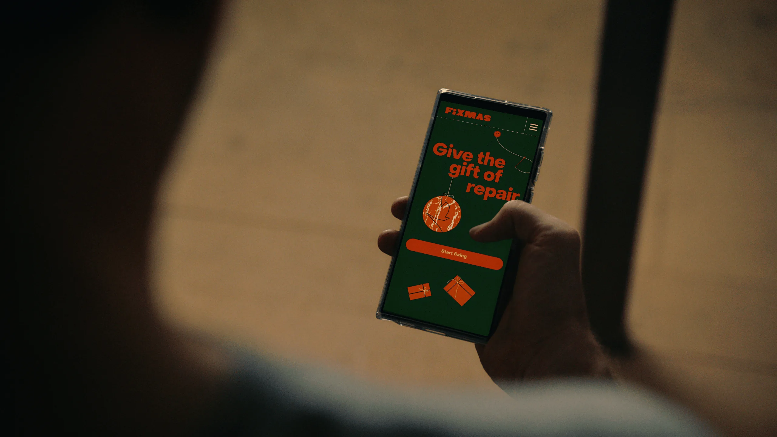 A person holds a smartphone displaying a green screen with orange text that reads Give the gift of repair, featuring a Buy Gift Card button and small gift icons.