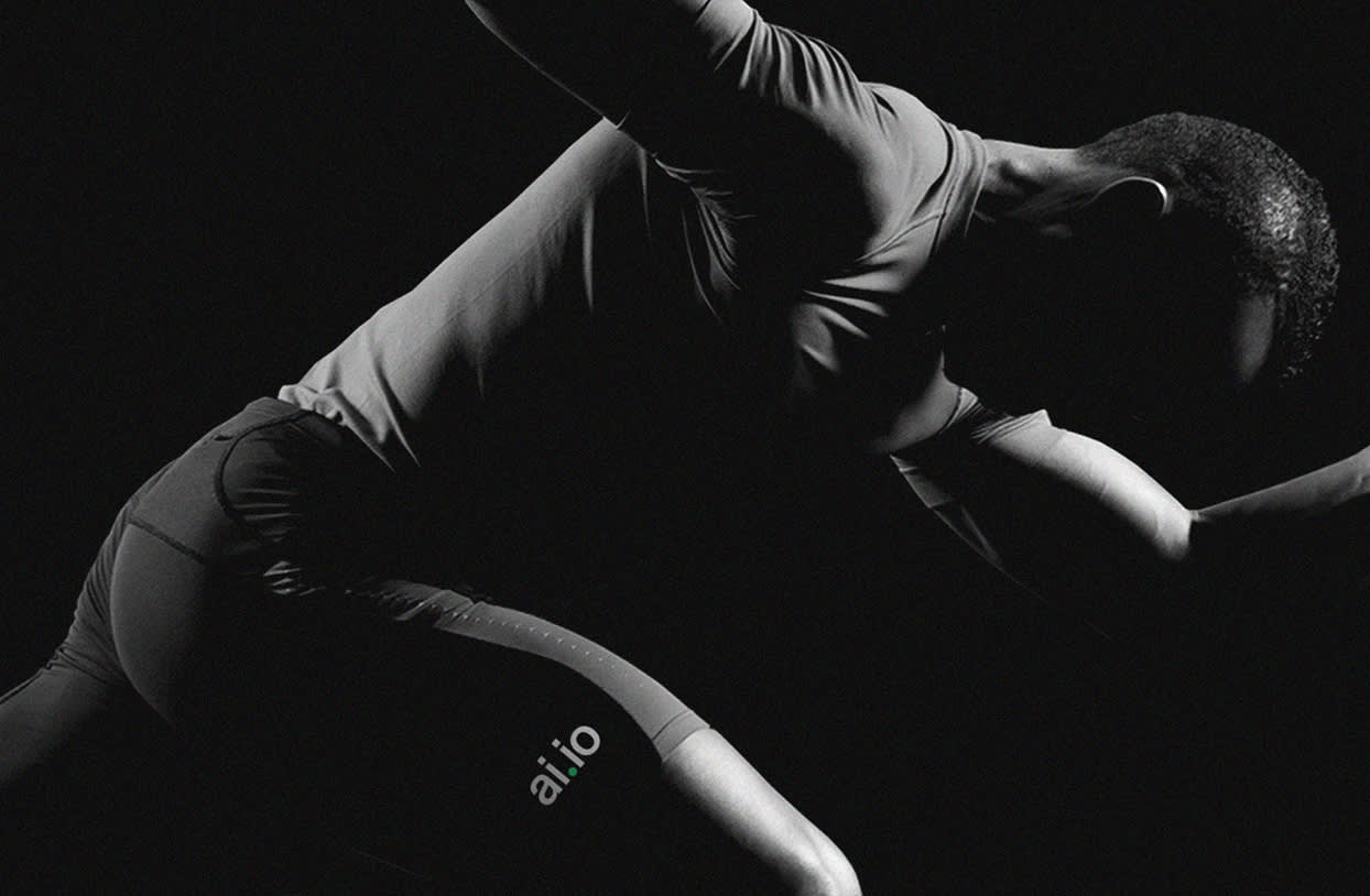 A male athlete in tight sportswear, marked with ai.io, is posed in a dramatic runner’s starting position, lit with strong contrast against a black background.