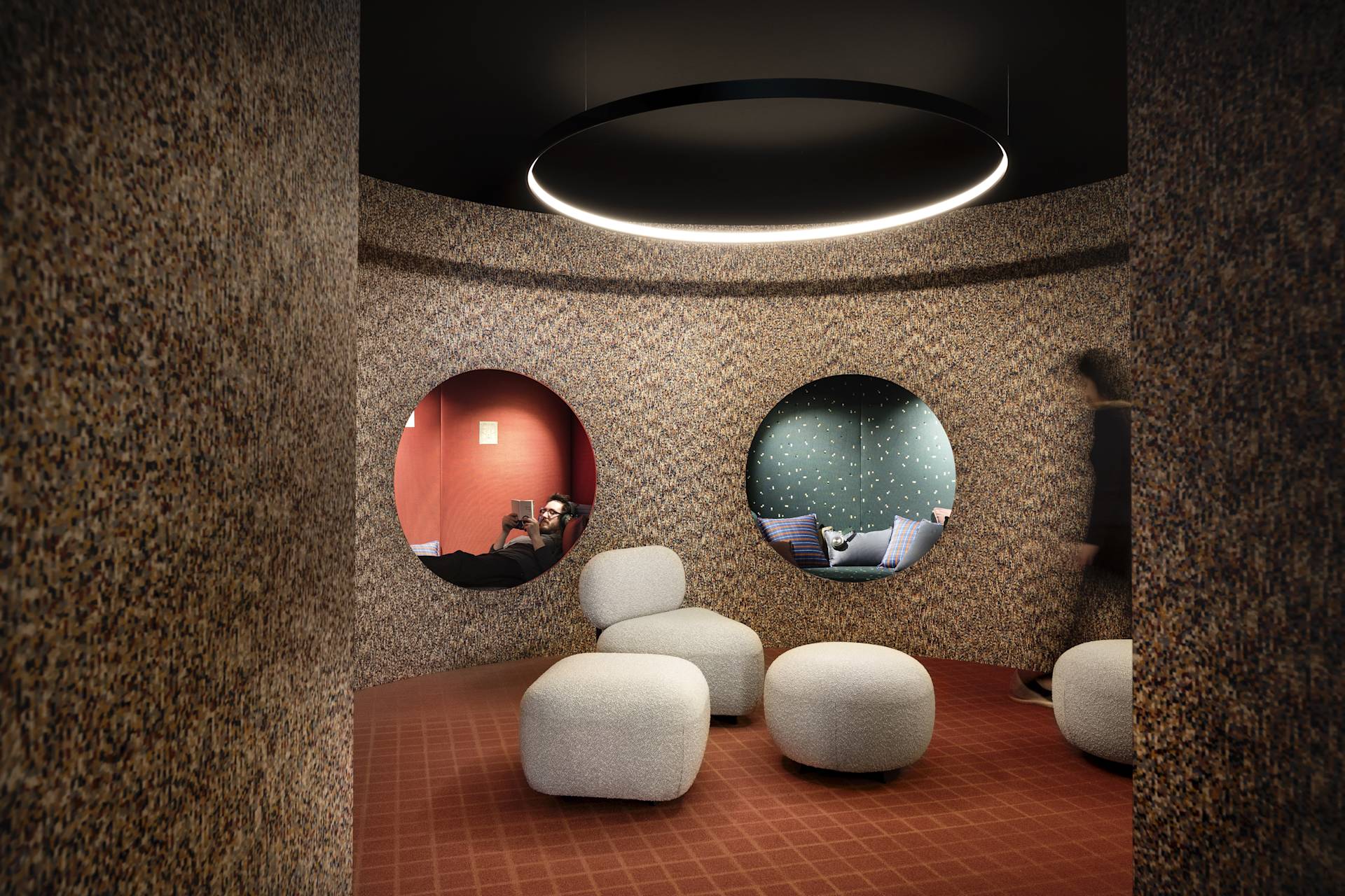 A modern lounge area with textured walls, circular openings revealing separate cozy nooks with seating, and soft rounded ottomans in the center under a large circular ceiling light.