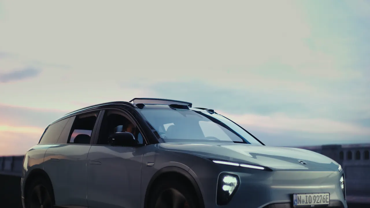 A modern silver SUV with headlights on is parked outdoors at dusk, with a cloudy sky in the background. The vehicles sleek design and illuminated features are prominent.