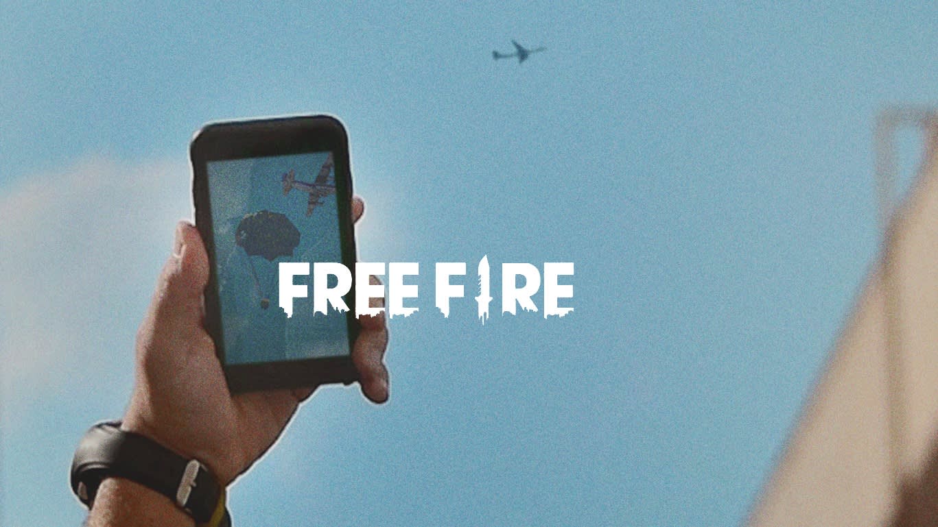 A hand holding a smartphone shows the Free Fire game on the screen, while in the background, a plane flies in the blue sky; the words FREE FIRE are displayed prominently in the center.
