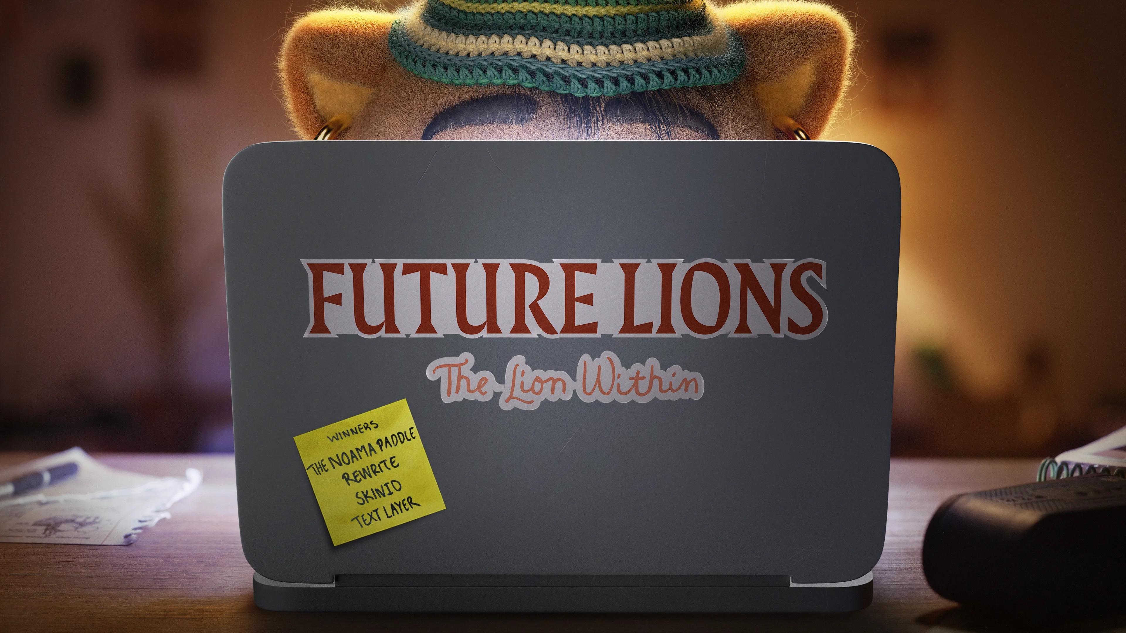 A person wearing a hat sits at a desk using a laptop with a sticker reading FUTURE LIONS The Lion Within. A yellow sticky note on the laptop says, THE NOMANA ARTICLE REMINDE SEND TO TEXT LATER.