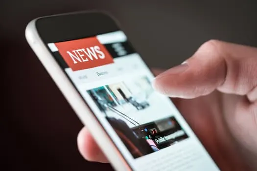 A person using a smartphone to read news online; the screen displays the word NEWS at the top with articles and images below.