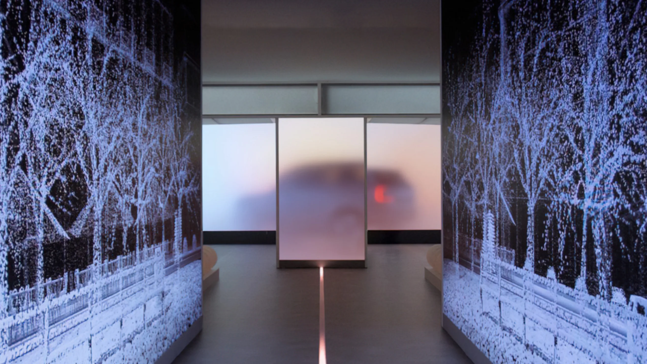 A blurred vehicle is seen through a frosted glass panel at the end of a modern hallway, with digital blue tree patterns displayed on dark walls on both sides.