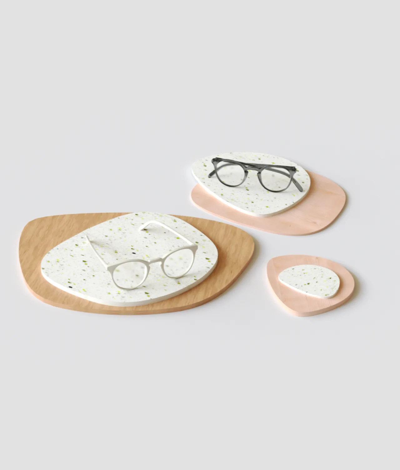 Three pairs of eyeglasses are displayed on terrazzo-patterned and wooden trays of varying sizes, arranged on a light gray background.