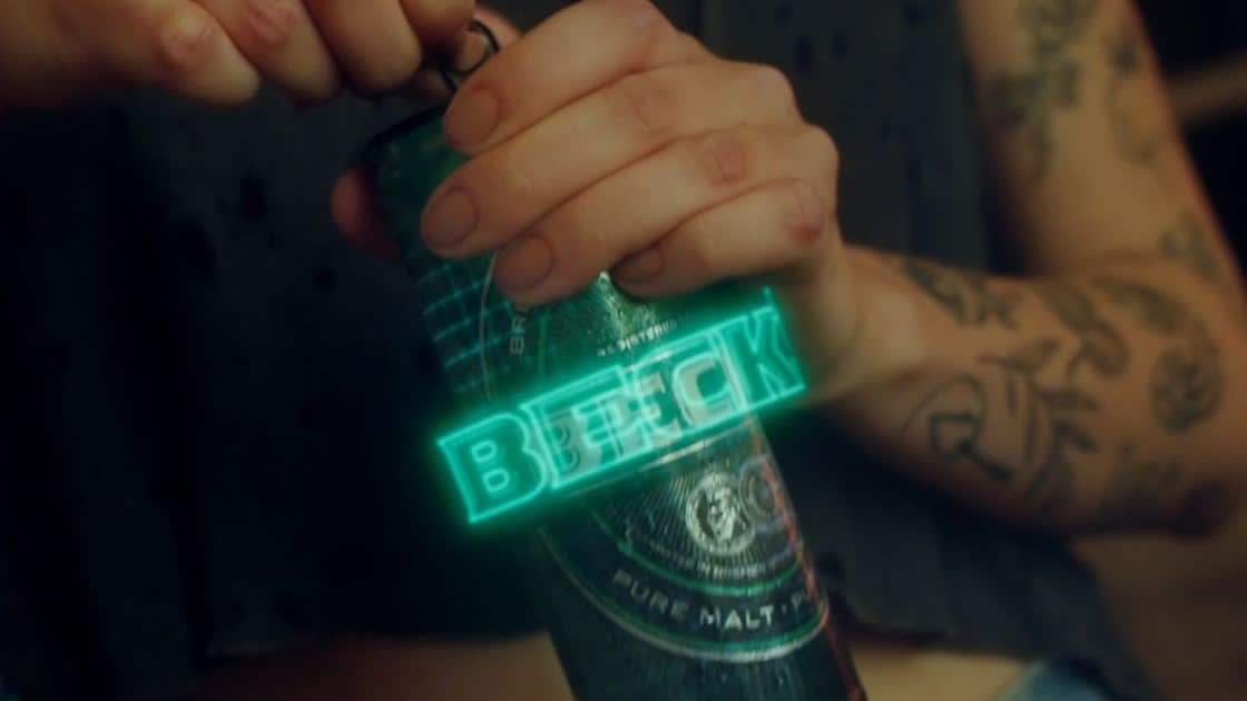 A person with tattooed arms opens a can of beer labeled BECK with a glowing neon effect over the logo.