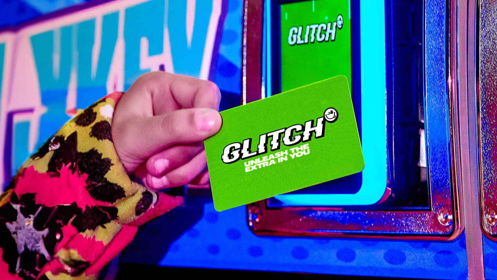 A hand holds a bright green GLITCH card up to an illuminated card reader. The card displays the text GLITCH UNLEASH THE EXTRA IN YOU. The background is colorful with blue and multicolored patterns.