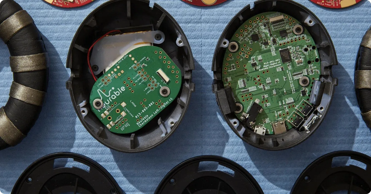 Close-up of two open electronic devices showing green circuit boards and components inside black plastic cases, placed on a blue surface.