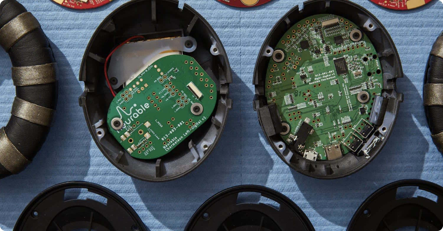 Close-up of two open electronic devices showing green circuit boards and components inside black plastic cases, placed on a blue surface.