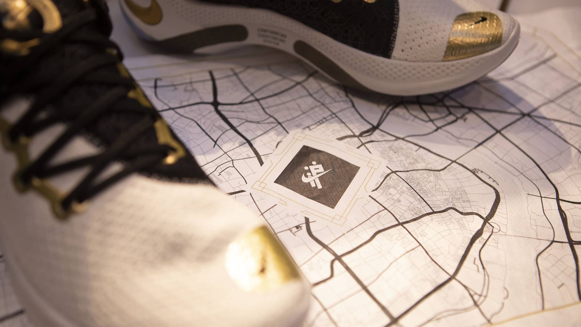 Close-up of white sneakers with gold and black accents placed on top of a city street map, with the shoes partially covering the map’s center design.