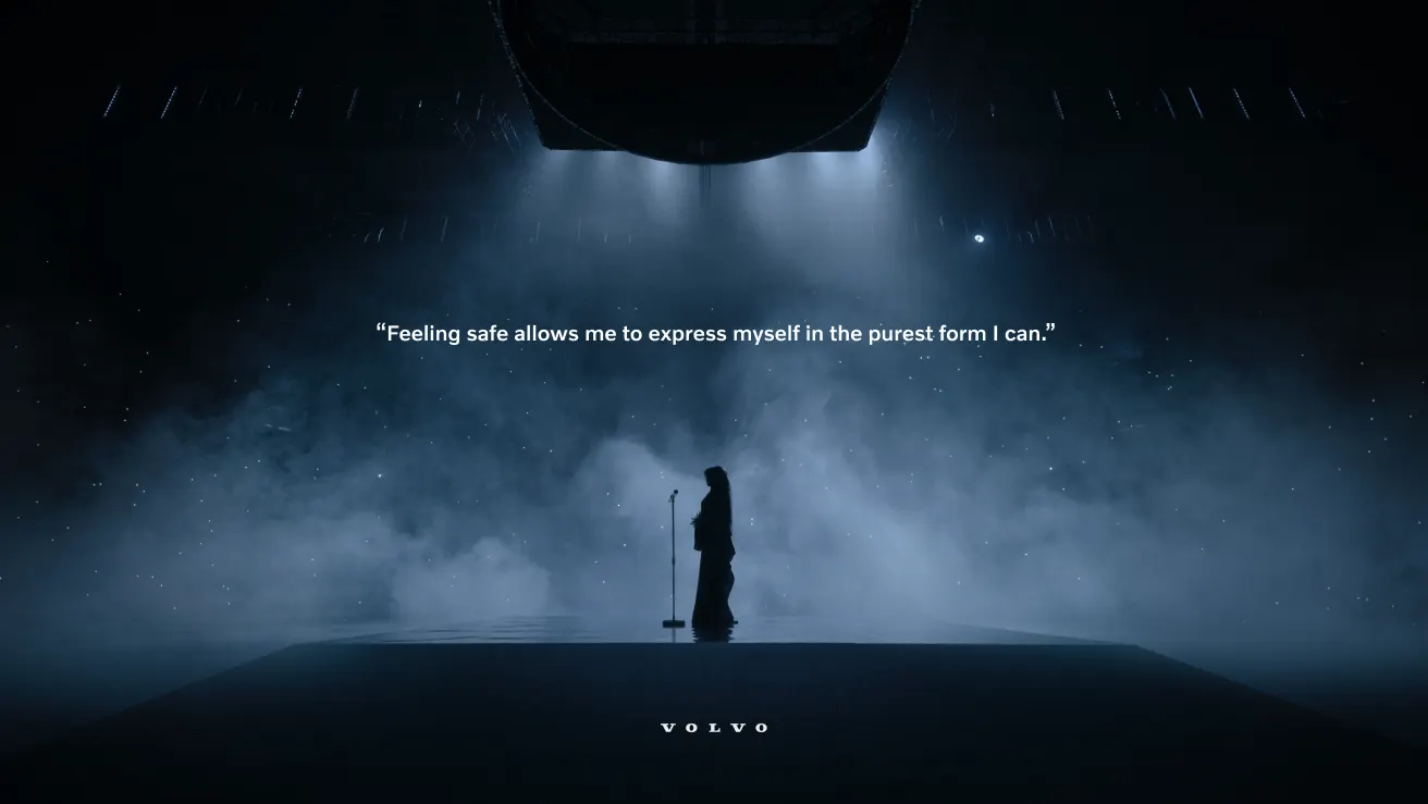 A person stands alone on a dimly lit stage with a microphone, surrounded by mist. Text above reads, Feeling safe allows me to express myself in the purest form I can. The Volvo logo appears at the bottom.
