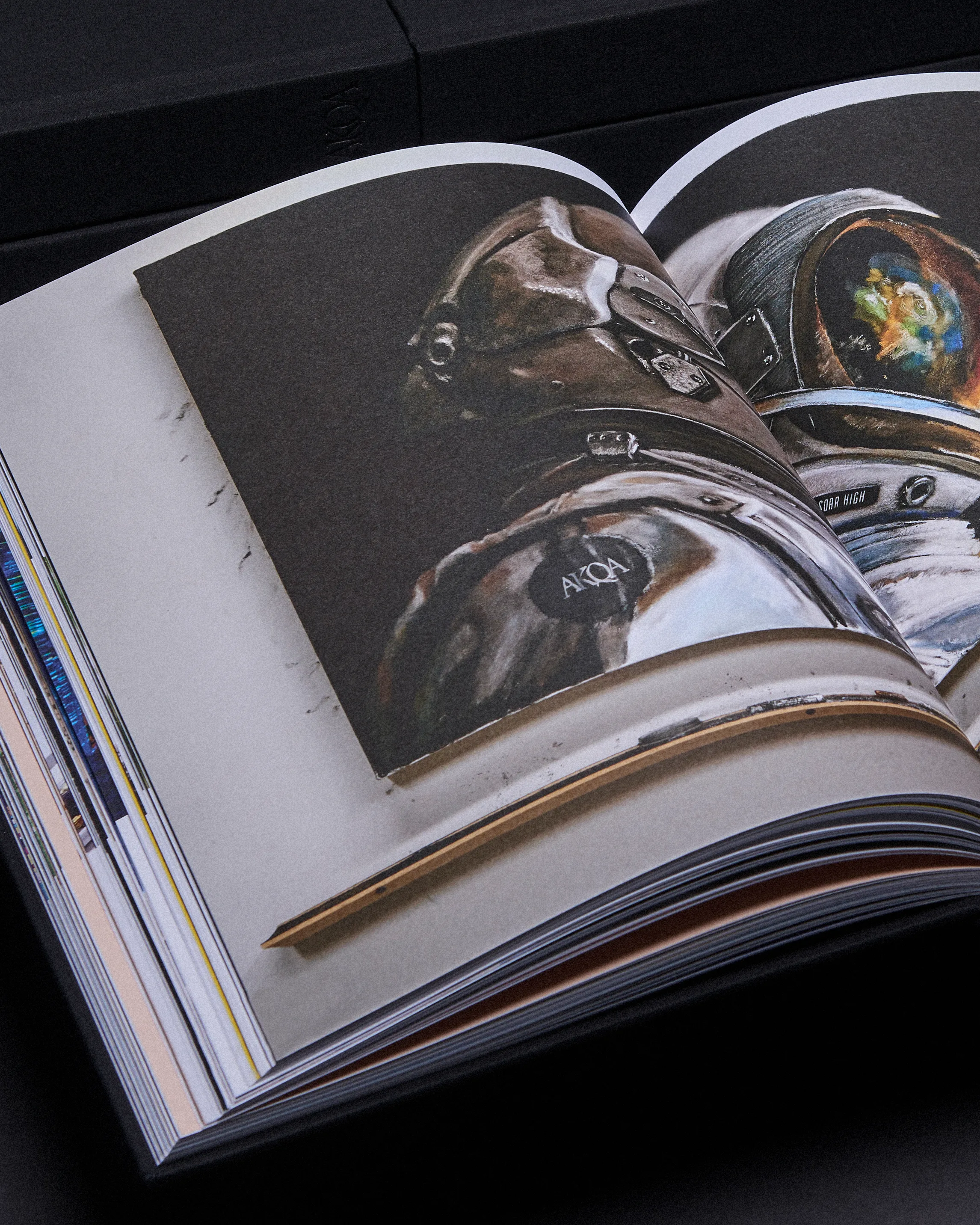 An open book displays an illustration of an astronaut in a spacesuit, with a pencil resting on the pages. The background is dark, and other books are partially visible.