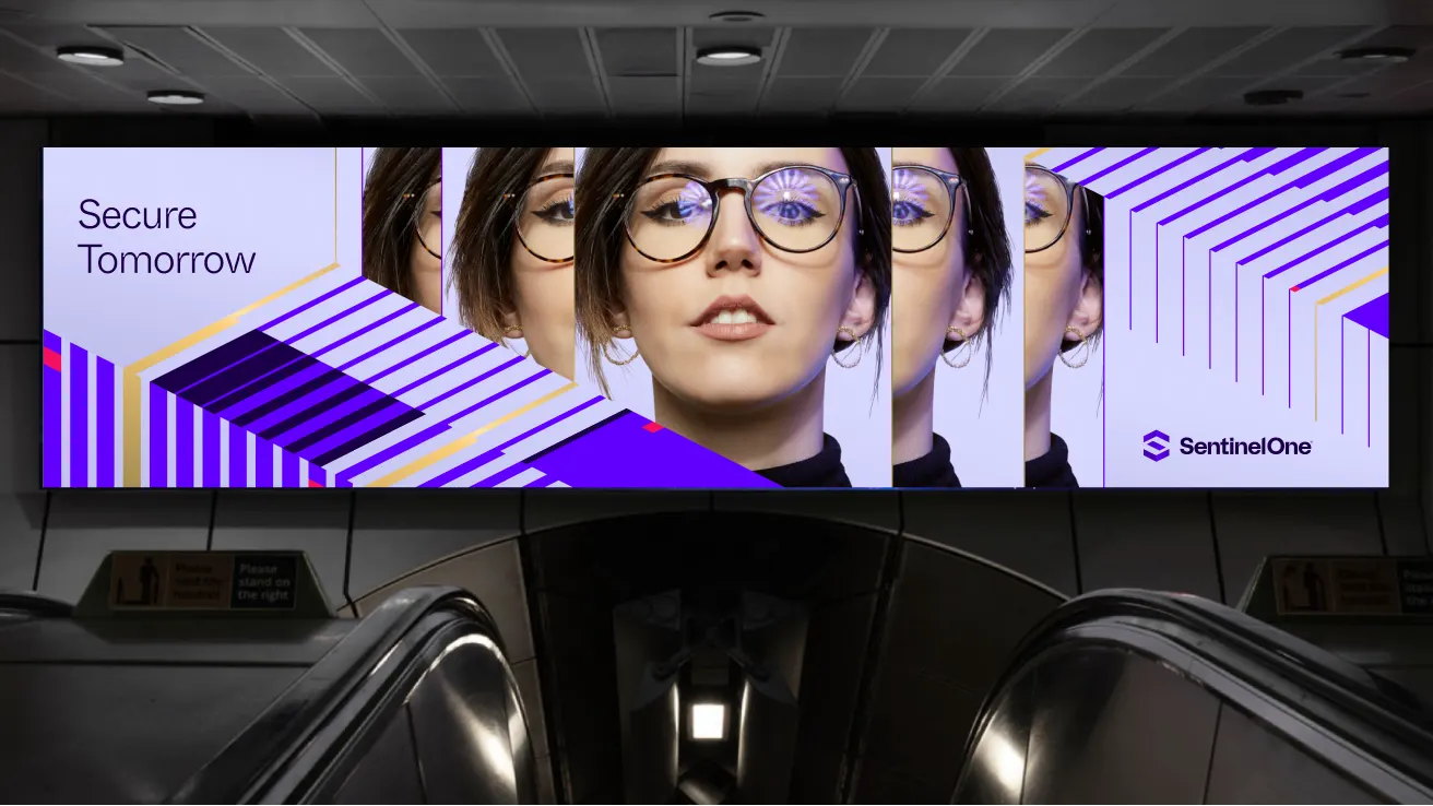 Digital billboard above escalators displays a repeating image of a woman in glasses with geometric purple patterns. Text reads Secure Tomorrow and features the SentinelOne logo.