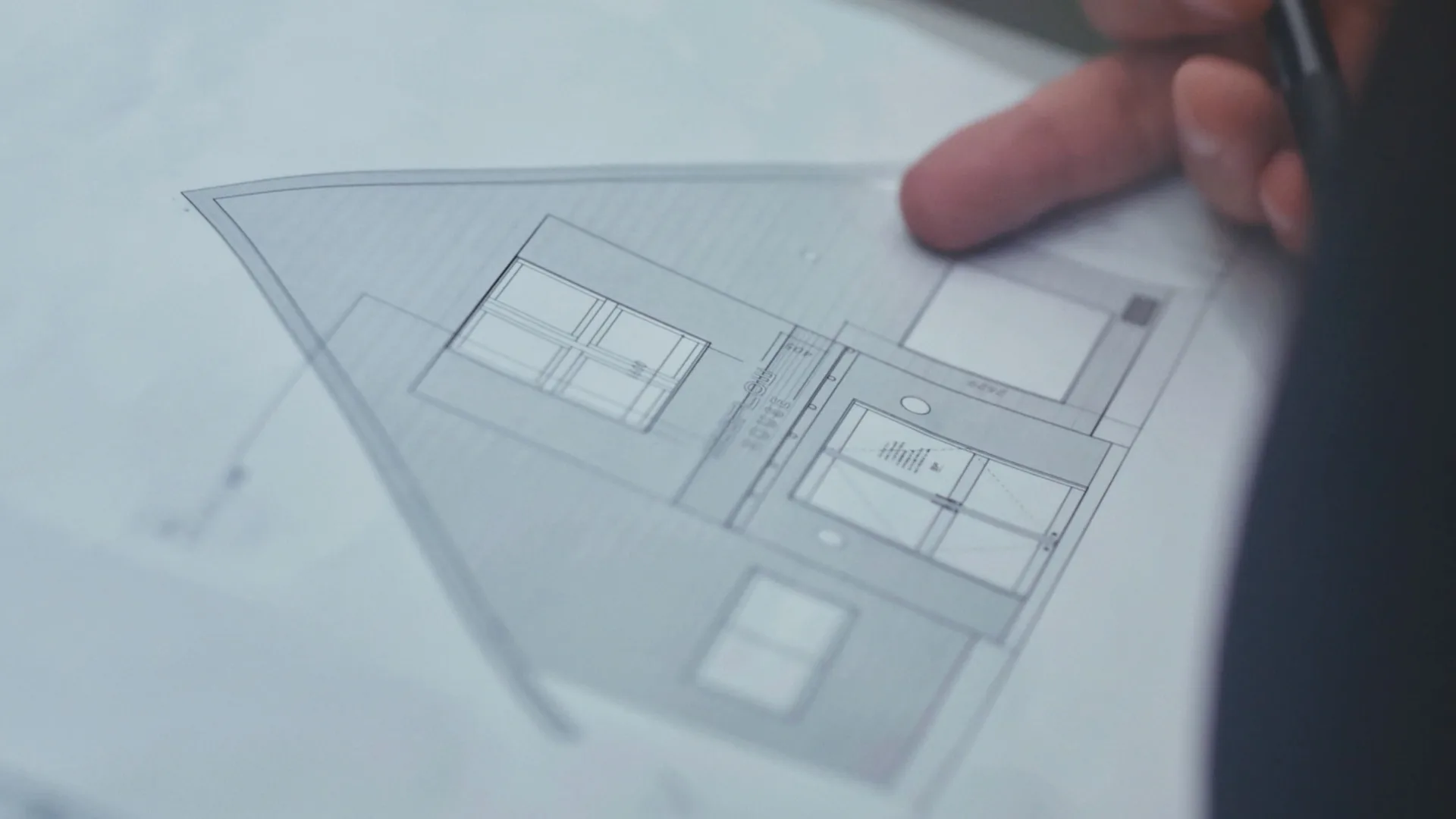 A close-up of a persons hand pointing at an architectural blueprint of a house, showing the buildings front elevation with windows and a door.