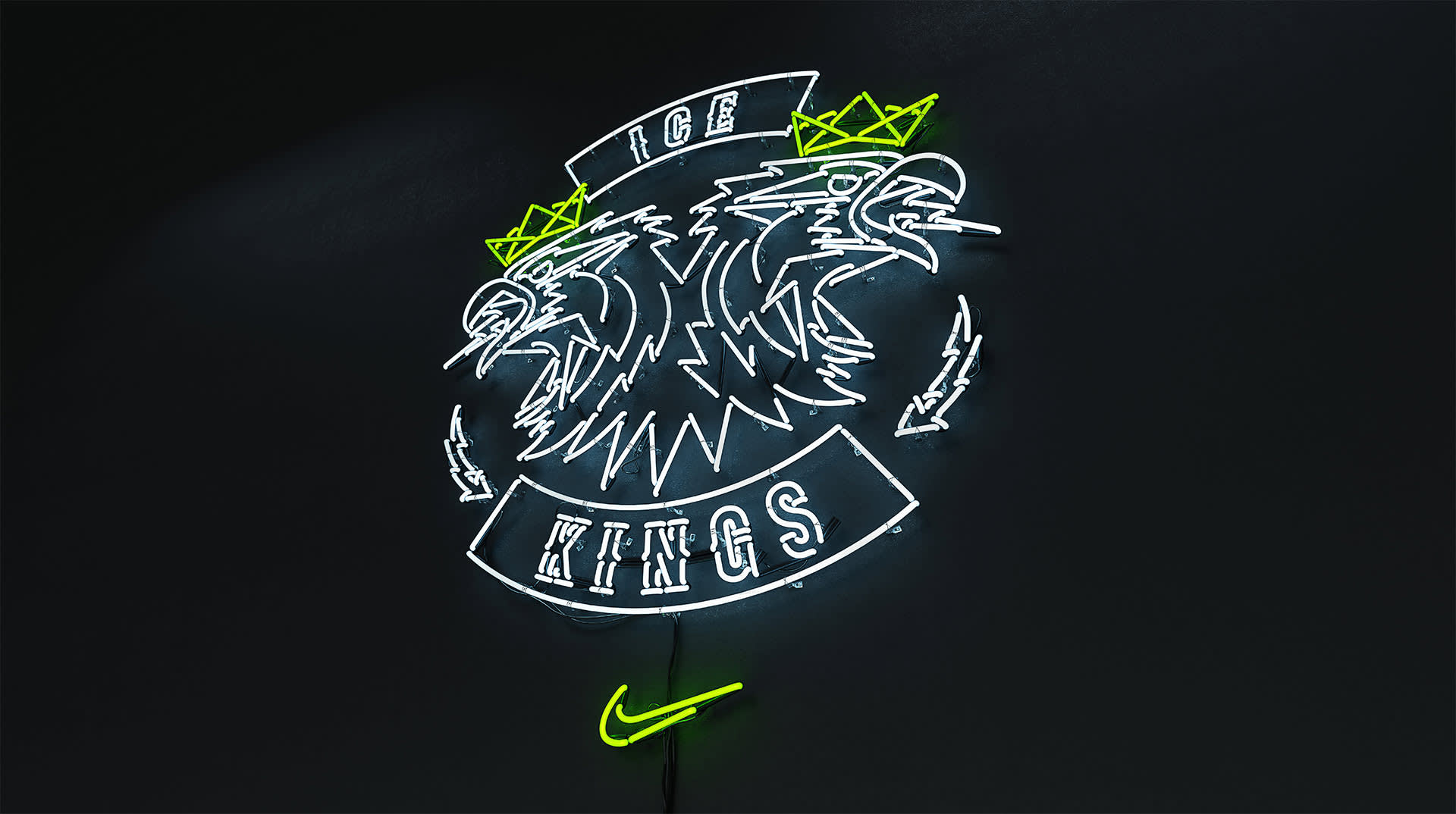 Neon sign of two eagle heads with yellow crowns and banners reading ICE above and KINGS below, with a yellow Nike swoosh at the bottom, glowing on a dark wall.