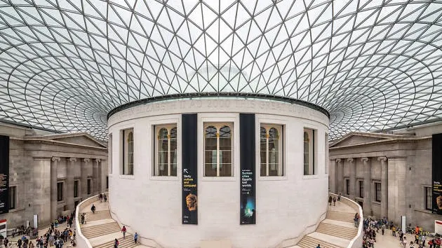 Wide view of the British Museum’s Great Court, featuring a white circular reading room surrounded by a glass roof and sweeping staircases, with visitors walking around the spacious, airy interior.