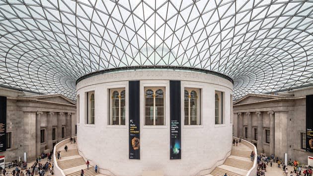 Wide view of the British Museum’s Great Court, featuring a white circular reading room surrounded by a glass roof and sweeping staircases, with visitors walking around the spacious, airy interior.
