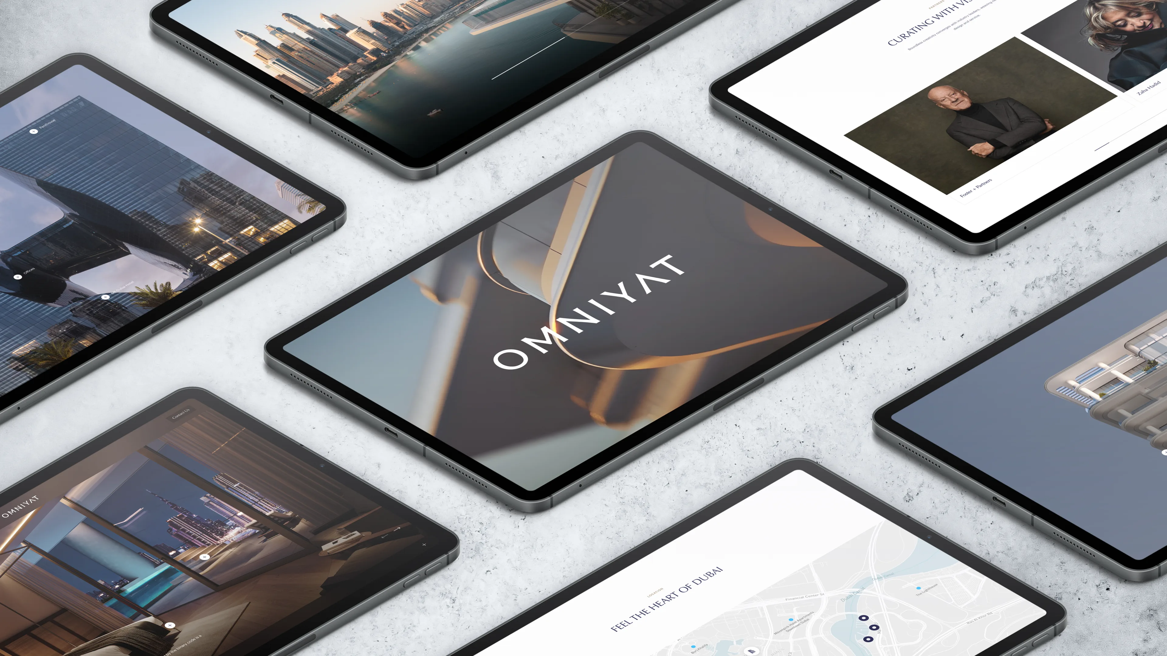 A top-down view of several tablets on a light surface, displaying modern website designs, architectural images, and the word OMNIYAT on the central tablet’s screen.