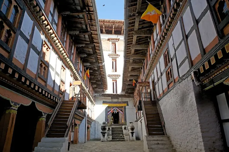 Traditionele Bhutaanse architectuur met karakteristieke houten balkons en decoratieve elementen in een smal steegje met centrale tempel en geel vlaggetje.