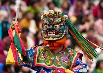 Een danser in traditioneel Bhutaans kostuum met een kleurrijke, indrukwekkende demonische masker voert een rituele dans uit tijdens een festival voor een groot publiek.