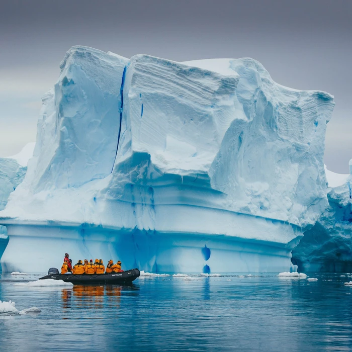 Een avontuurlijke zodiac-excursie voert toeristen in gele reddingsvesten langs imposante ijsbergen met diepblauwe spleten in de poolwateren van Antarctica.
