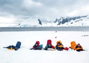 Een groep avonturiers ligt ontspannen in de sneeuw voor een adembenemend uitzicht op besneeuwde bergen en gletsjers in Antarctica.