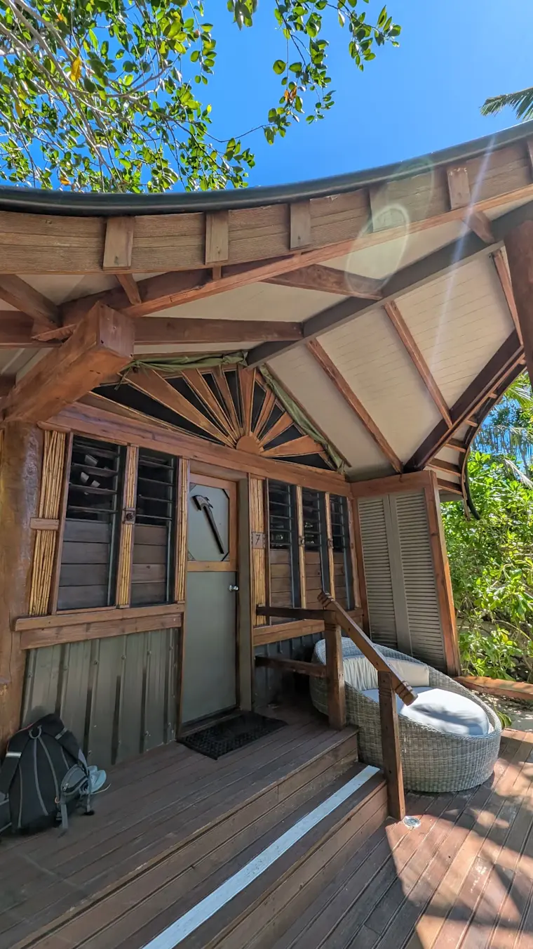 Een houten glamping-huisje met moderne airconditioning units en panoramische ramen onder een natuurlijke overkapping van bladeren en tropische vegetatie.