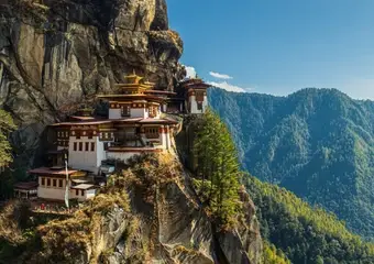 Het iconische Tigernest-klooster kleeft dramatisch aan een steile rotswand hoog in de groene bergen van Bhutan, met traditionele architectuur en gouden daken tegen een helderblauwe hemel.