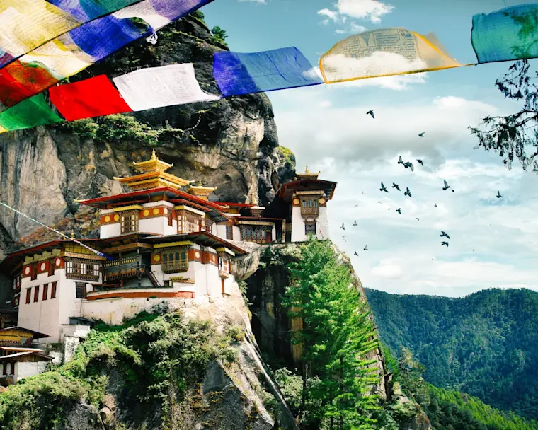 Het beroemde Taktshang-klooster, beter bekend als Tiger's Nest dat vastgeklampt zit aan de steile rotswand, met boeddhistische gebedsvlaggen op de voorgrond.