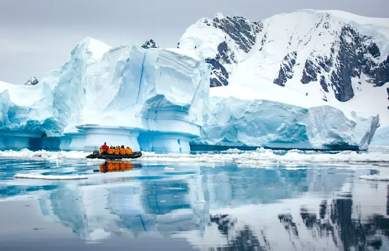 Een avontuurlijke expeditie in een gele rubberboot vaart langs imposante blauwe ijsbergen en besneeuwde bergtoppen in het polare landschap van Antarctica.