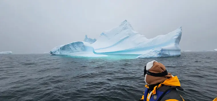Een avonturier in een kajak bewondert een majestueuze ijsberg met helderblauwe tinten drijvend in de koude poolwateren.