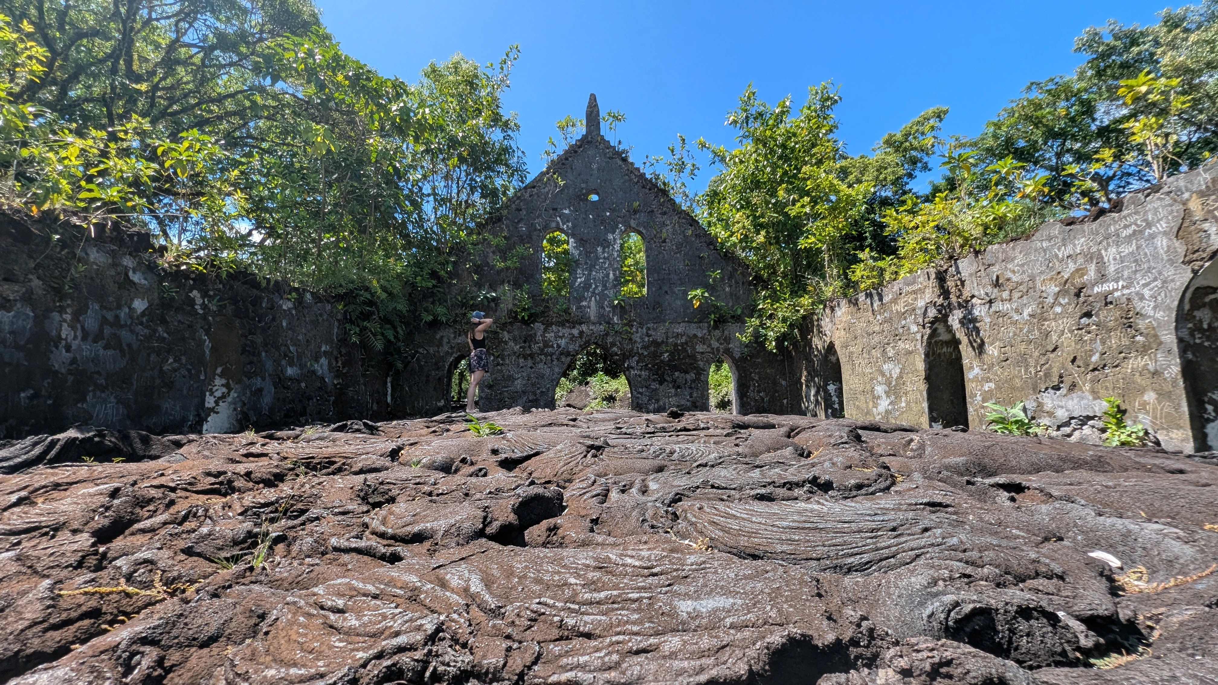 Mystieke ruïnes van een oude stenen kerk omgeven door weelderige groene vegetatie en zwarte vulkanische rotsen in een tropisch landschap in Samoa.