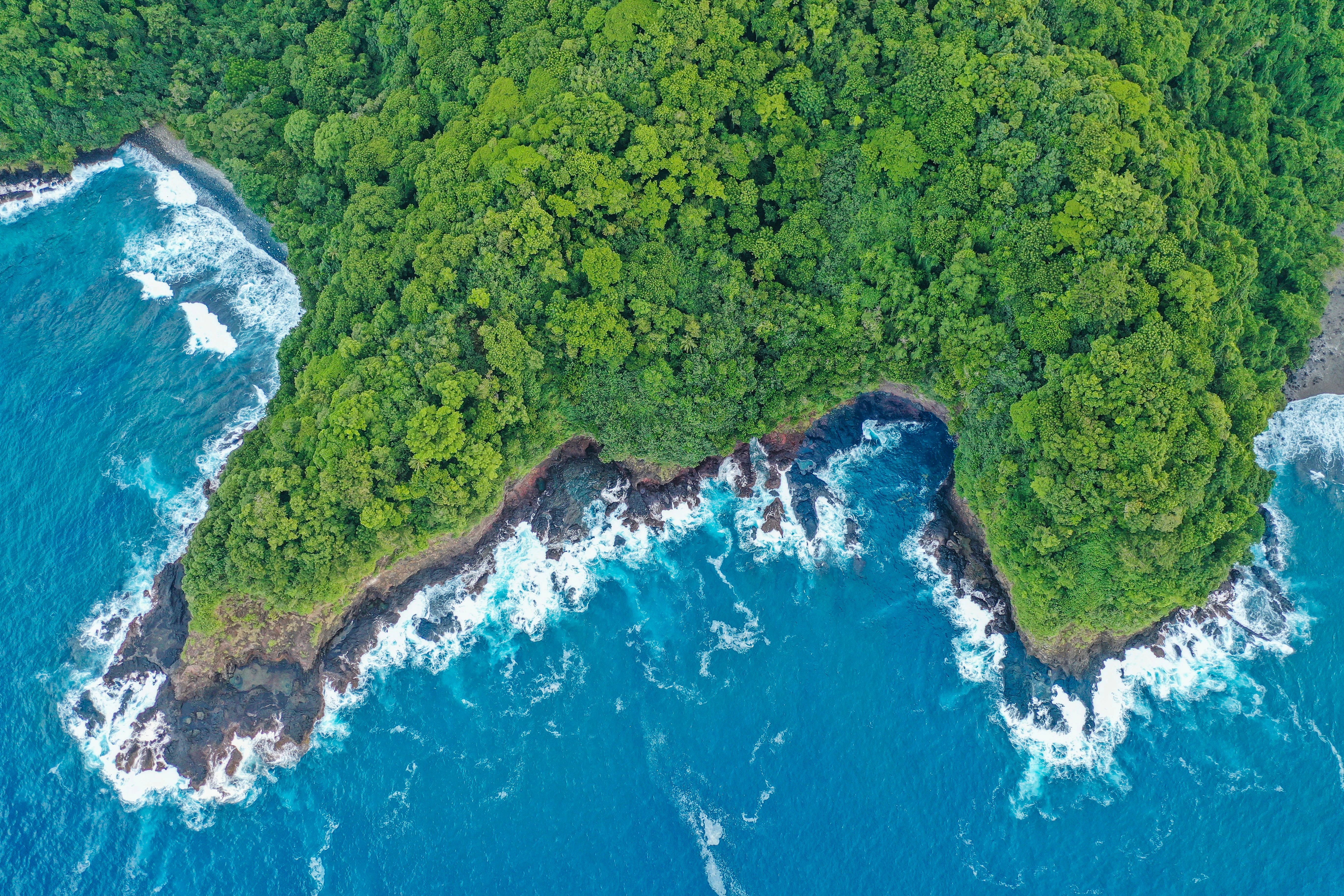 Spectaculair luchtfoto van een rotsachtig schiereiland omgeven door turquoise oceaanwater en bruisende golven, ingesloten door dicht tropisch regenwoud.