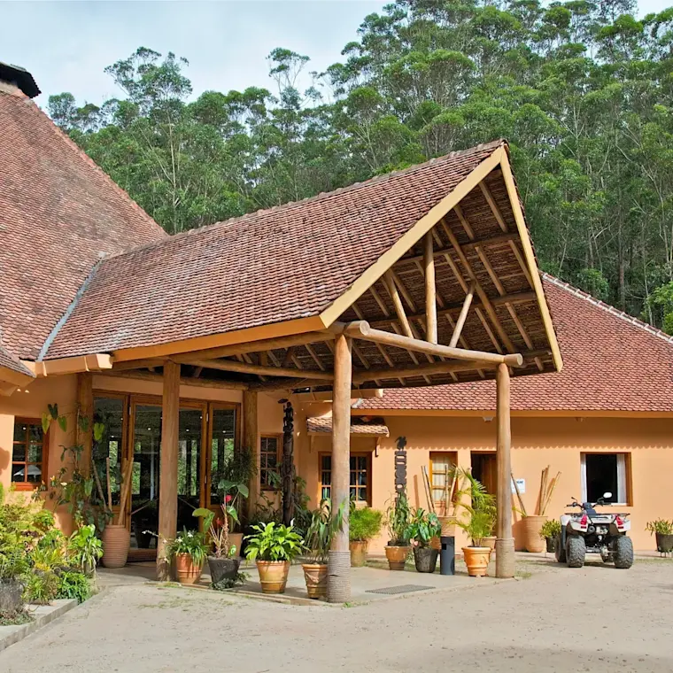 Een luxe houten villa met terracotta pannendak en grote houten overkapping, omgeven door tropische planten en eucalyptusbomen, uitstralend een serene en rustige sfeer.