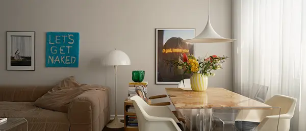 Ljust vardagsrum med matbord, stolar, soffa, designlampa och väggkonst i modern bostadsmiljö.