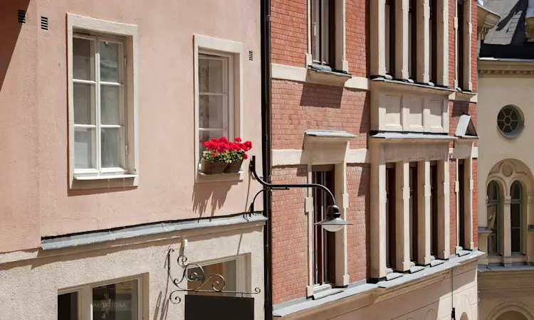 Tegelfasad på bostadshus med flera fönster och blomkruka som pryder fasaden.