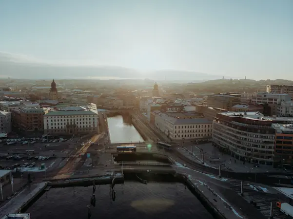 Flygvy över centrala Göteborg med kanal, bro, stadsbebyggelse och morgonljus över stadens takåsar.