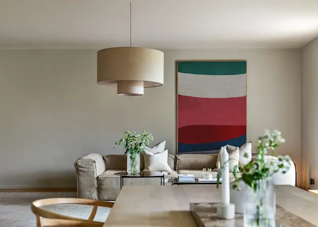 Ljust vardagsrum med soffa, soffbord, konst på väggen och stilren inredning i öppen planlösning.