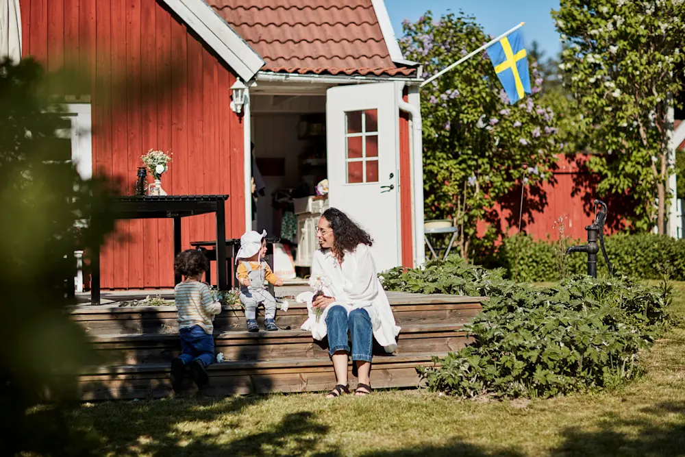 Röd villa med trappa och trädgård där flera personer vistas utanför huset, med svensk flagga vid entrén.