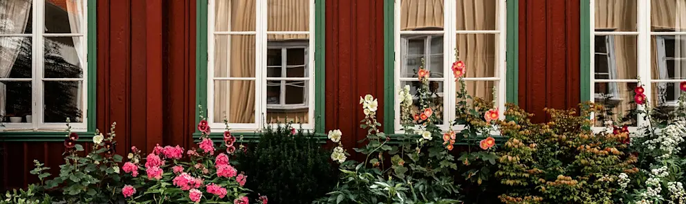 Röd träfasad med spröjsade fönster och blommande trädgård utanför ett traditionellt svenskt hus.