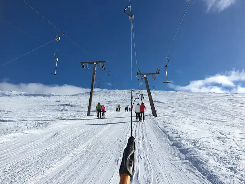 Skidlift i snötäckt fjällmiljö med skidåkare på väg uppför backen under klarblå himmel.