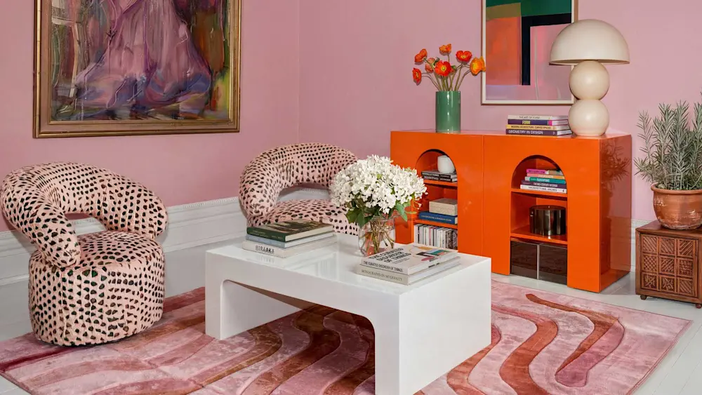 Stilfullt vardagsrum med rosa väggar, färgstark konst, mönstrade fåtöljer och modern inredning.