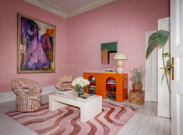 Stilfullt vardagsrum med rosa väggar, färgstark konst, mönstrade fåtöljer och modern inredning.